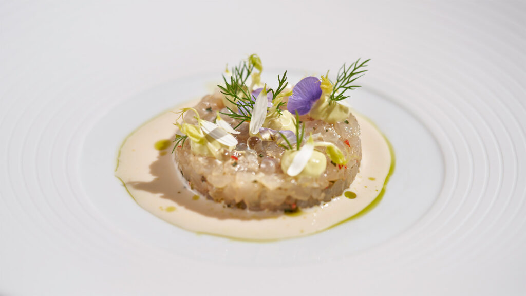 Tartare de poisson avec fleurs et herbes sur une assiette blanche.