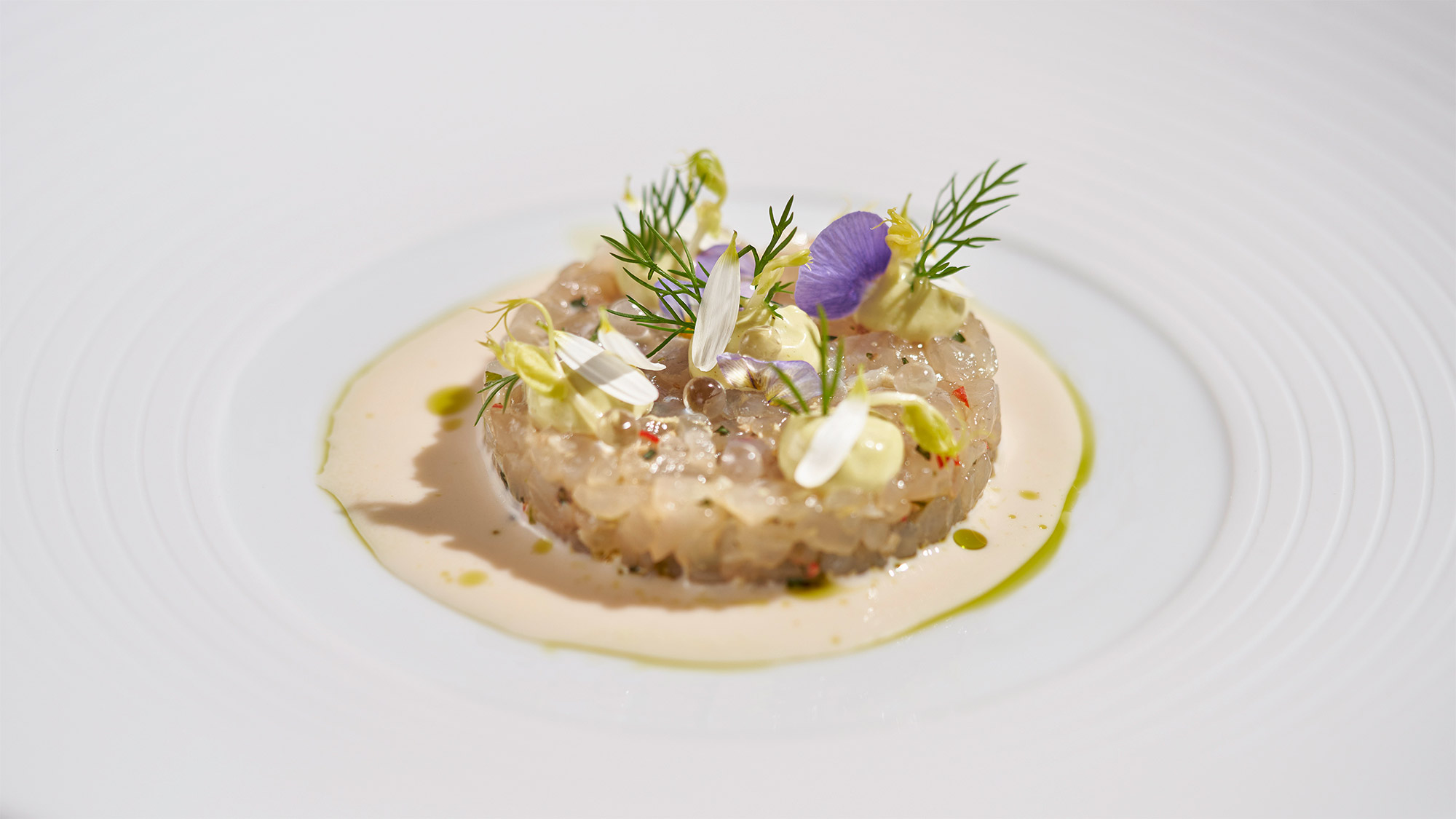 Fish tartare with flowers and herbs on a white plate.