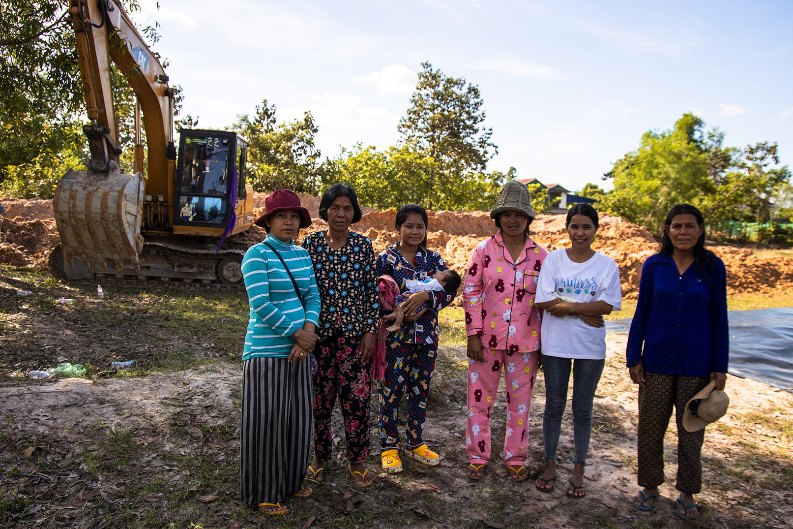 A group of women stands beside a fish-pond construction site.