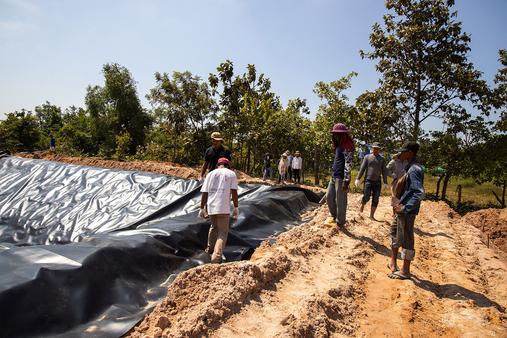 Several people stand beside a pond lined with sheeting.