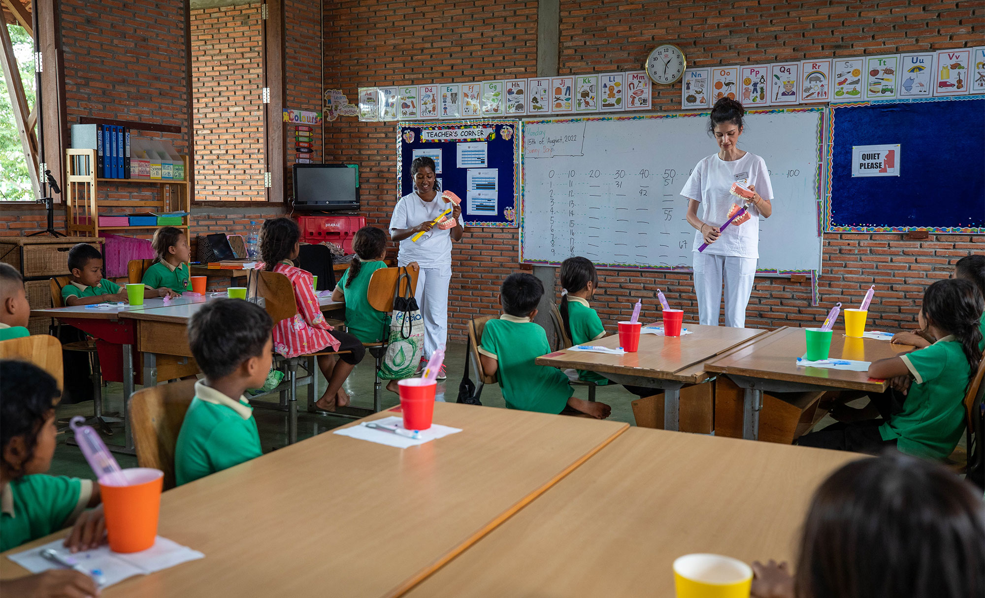 Eine Fachperson erklärt Schulkindern das Zähneputzen.