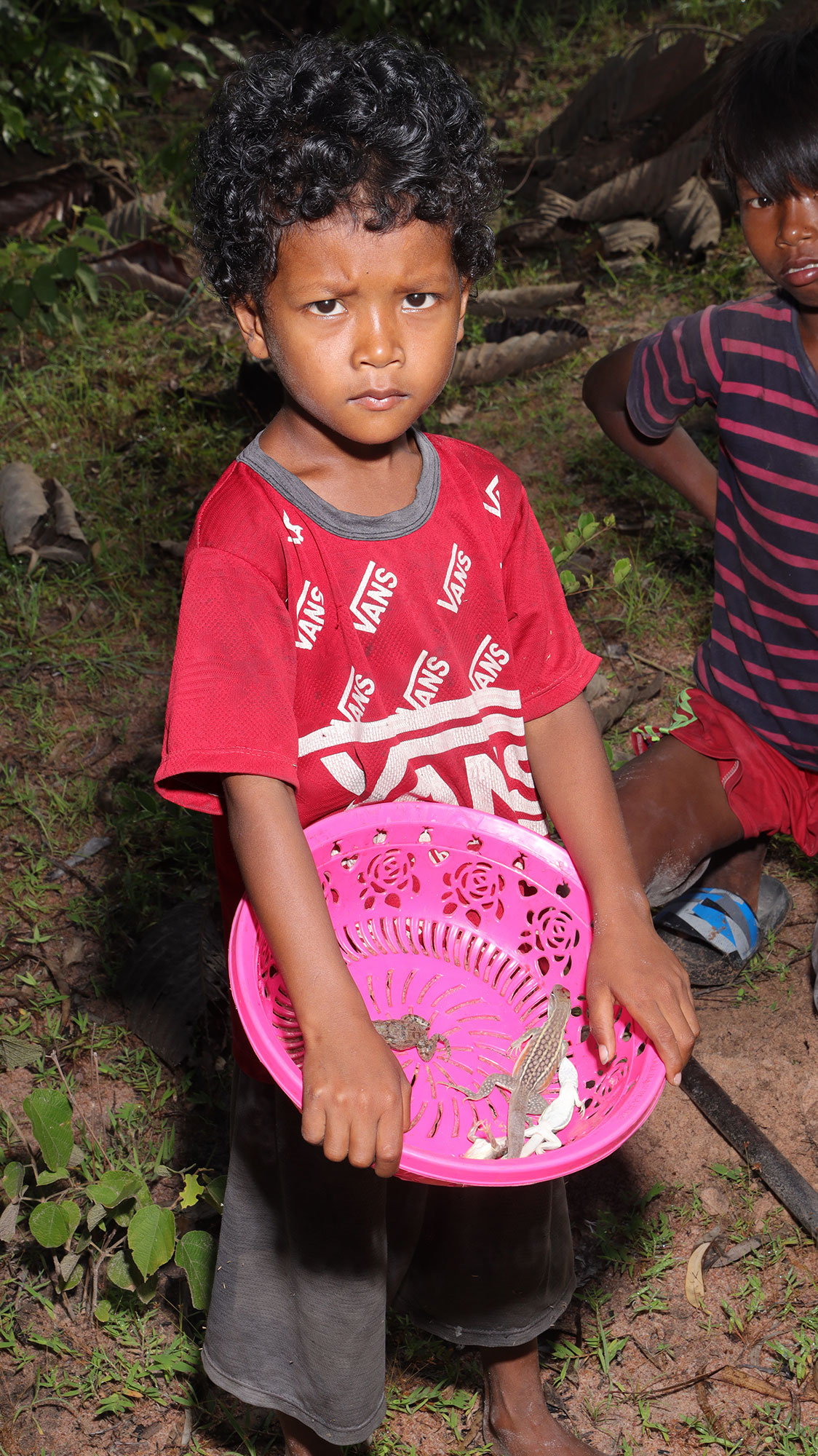 Un garçon en tee-shirt rouge tient une bassine rose.