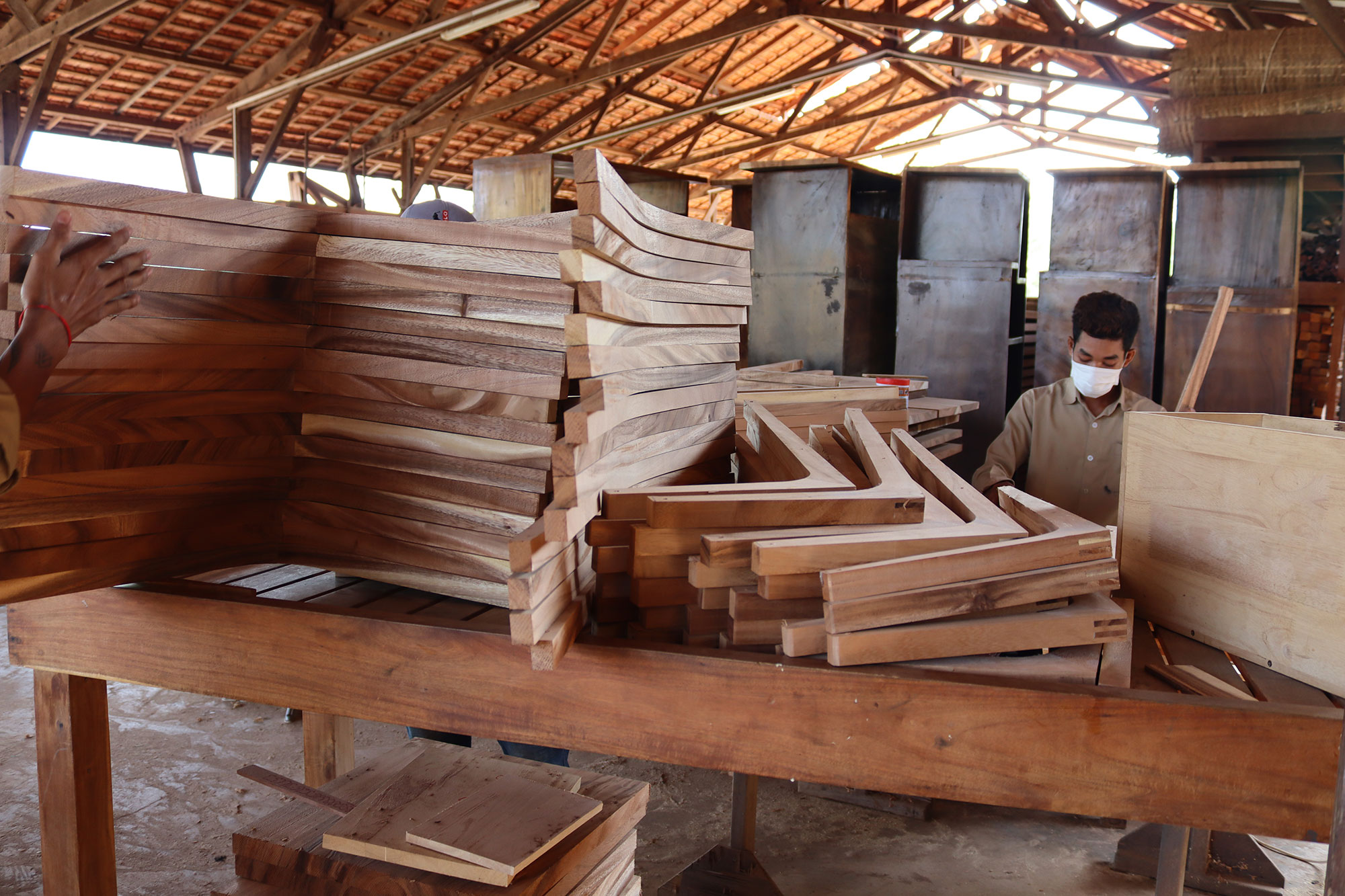 Un menuisier travaille entre des panneaux de bois et des éléments de mobilier.