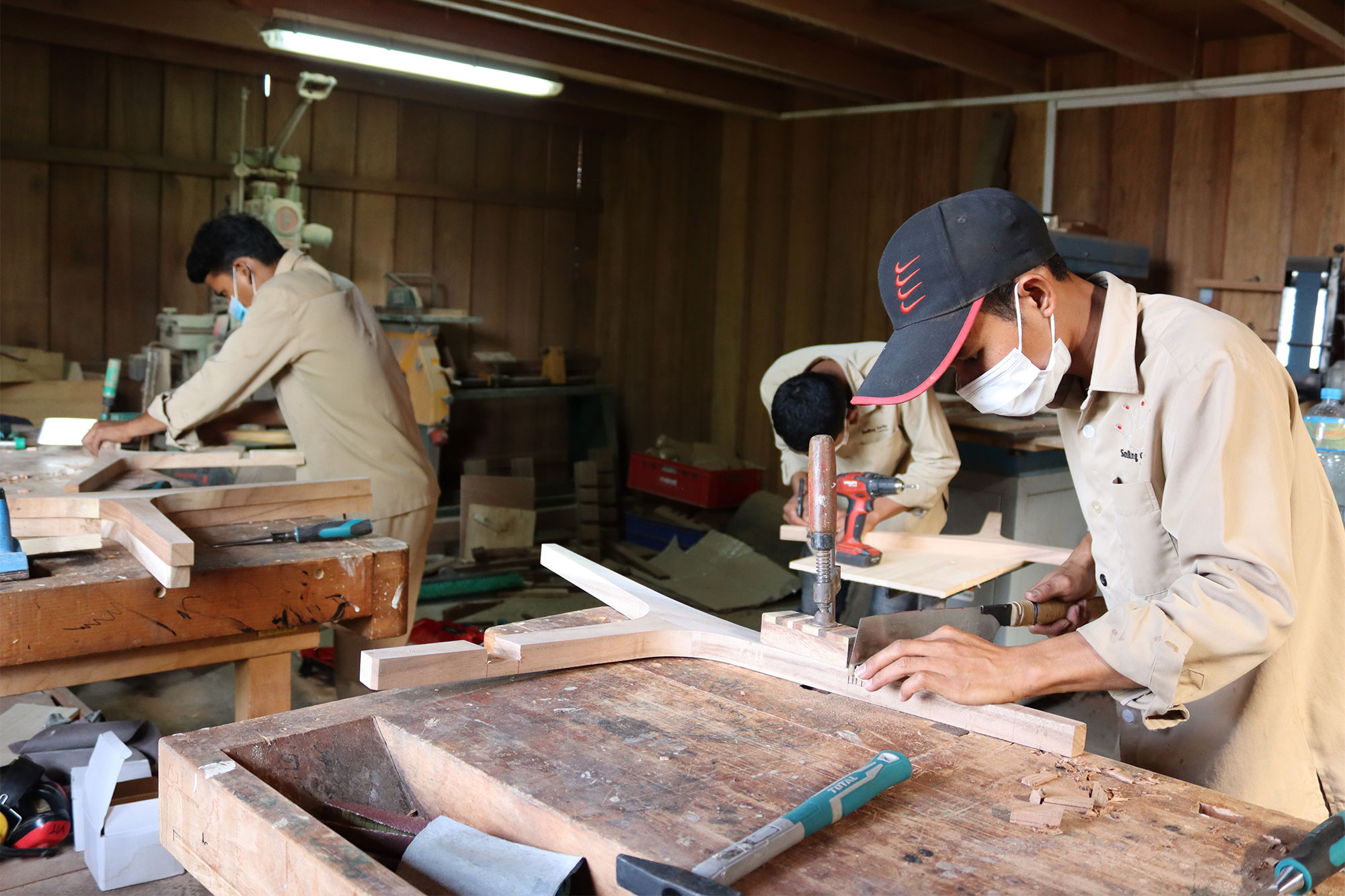 Des employés travaillent le bois sur des établis dans la menuiserie.