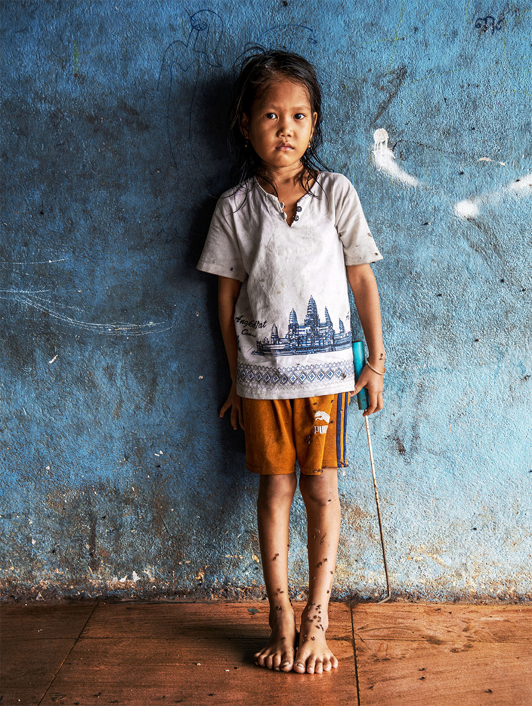 A girl stands barefoot in front of a blue wall.