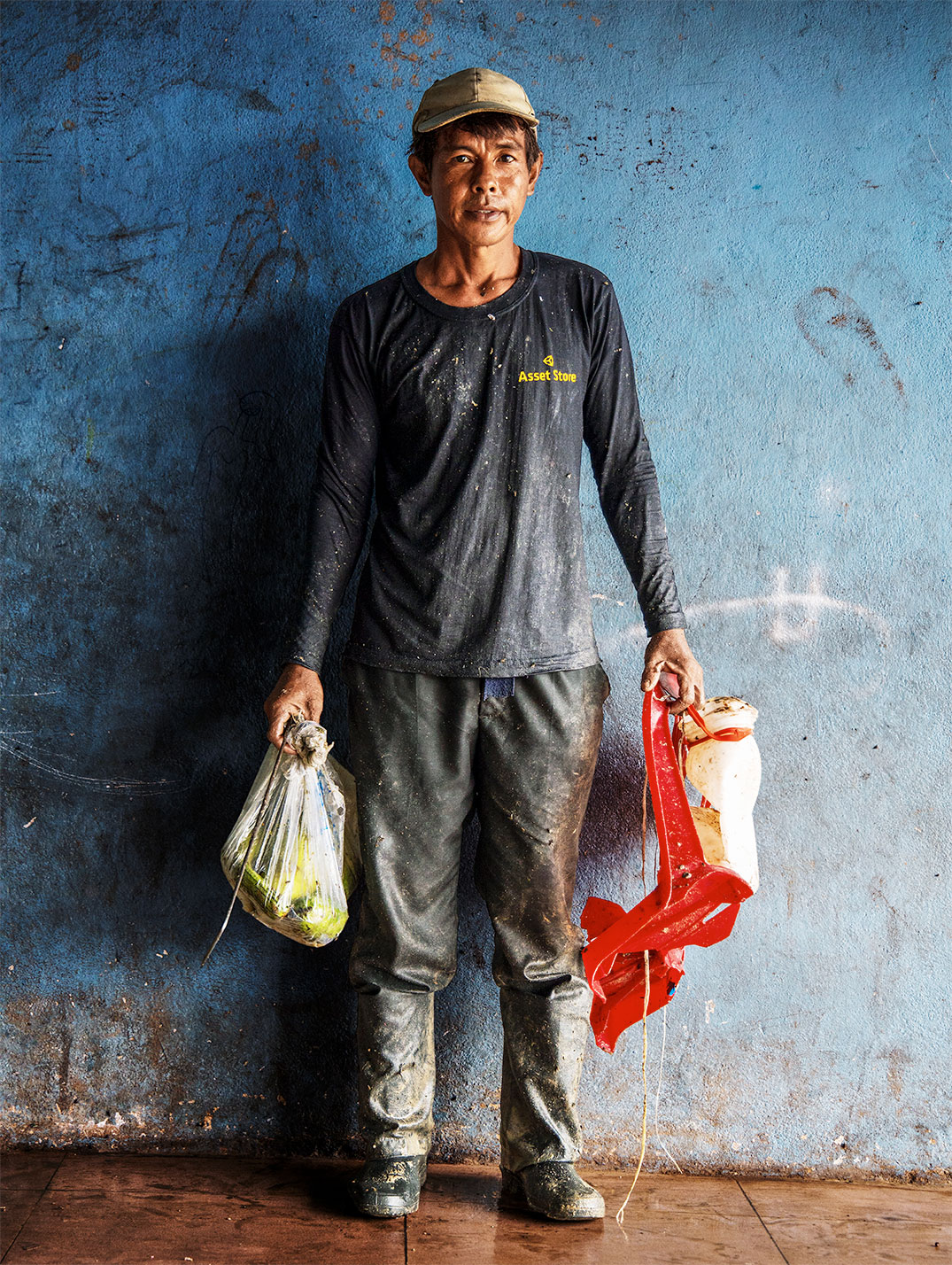 A man stands holding bags in front of a blue wall.