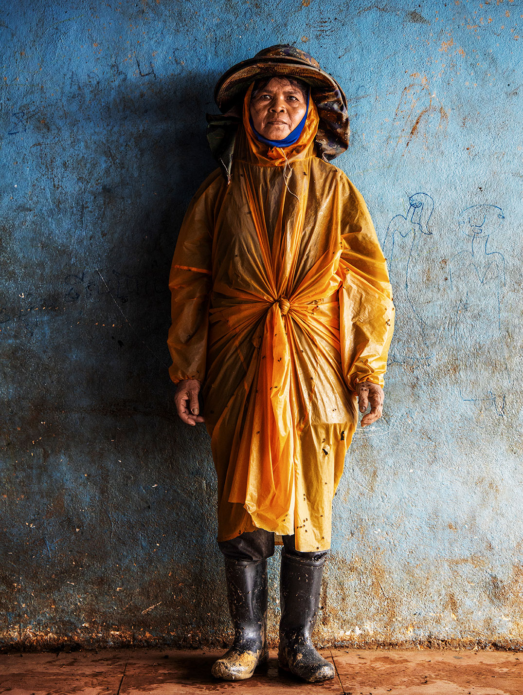 A woman wearing yellow stands in front of a blue wall.