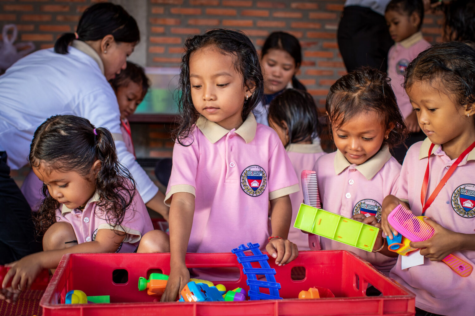 Kinder in rosa Uniformen wählen Spielzeug aus einer roten Kiste.