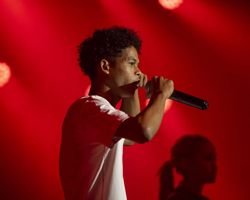 Un chanteur au micro sur la scène éclairée en rouge du Gong.