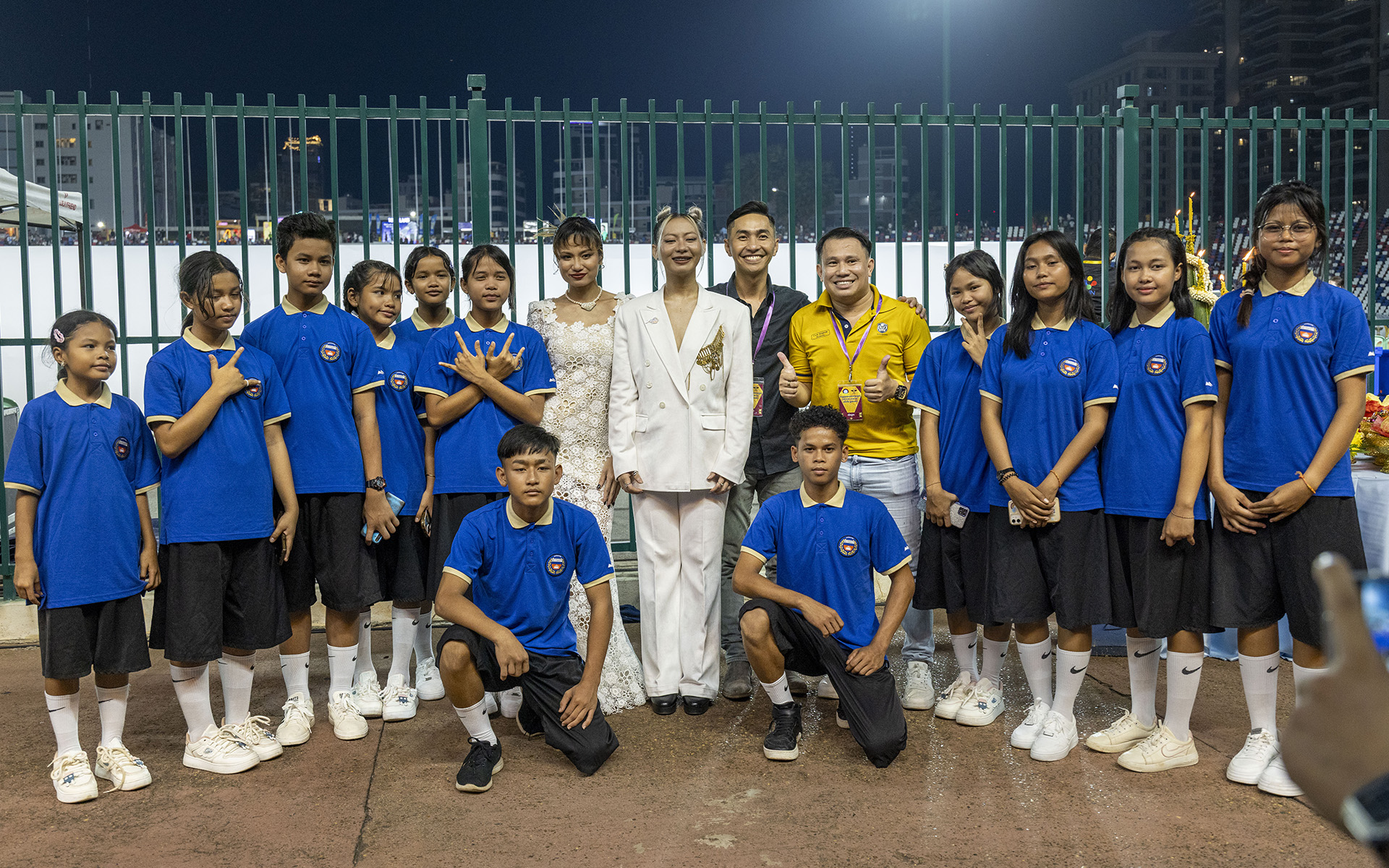 Group photo of schoolchildren and accompanying adults at the stadium.