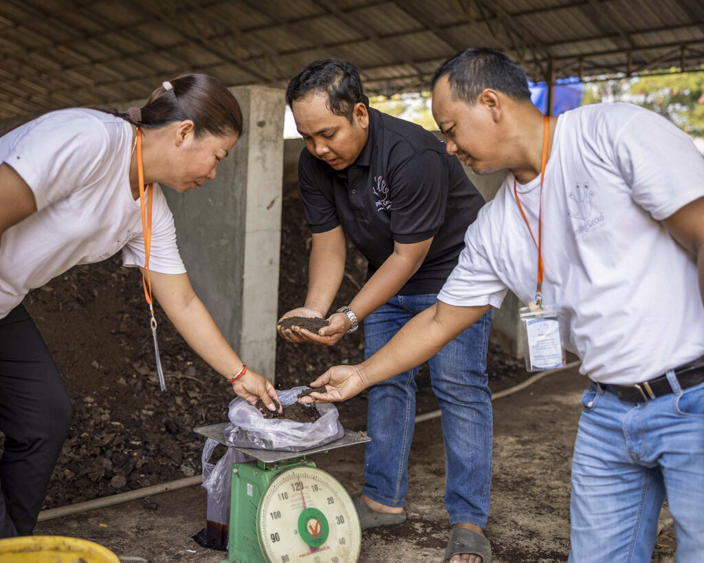 Three men weighing a sack together on a scale.