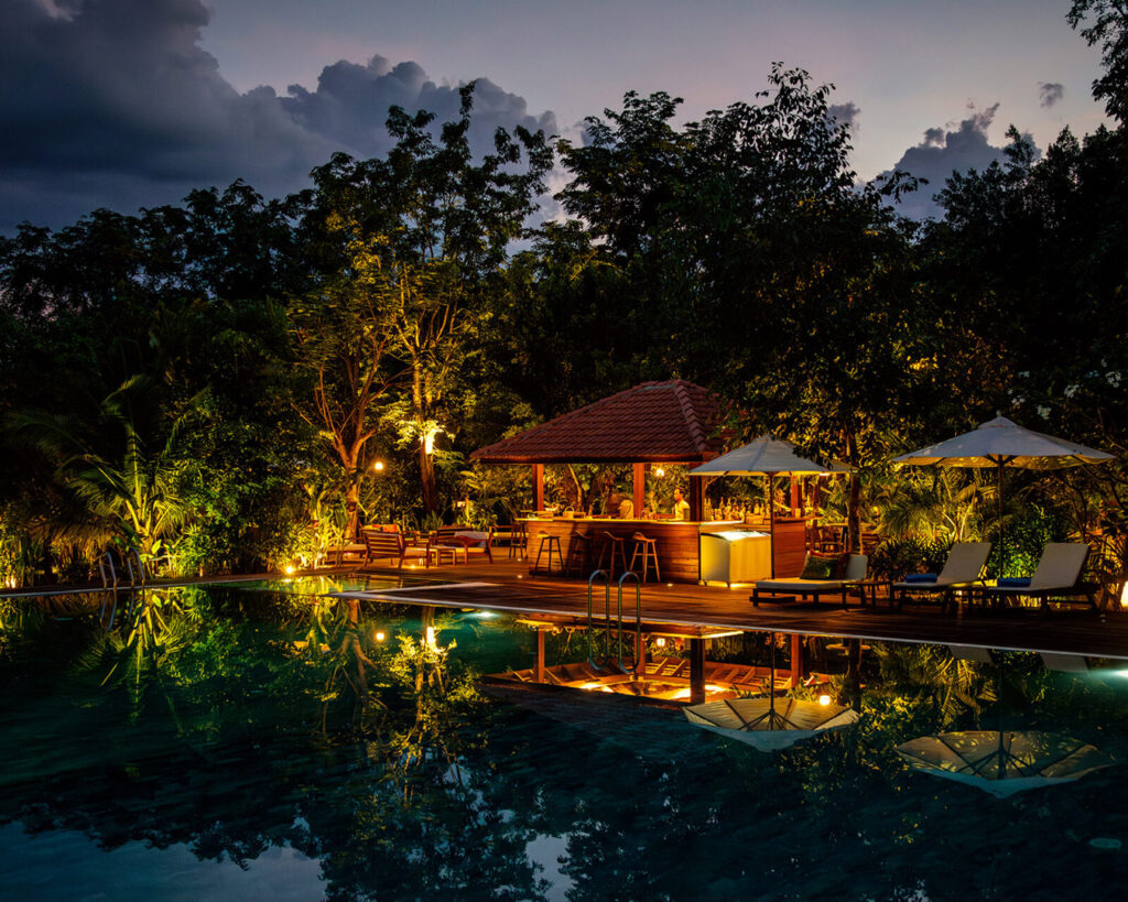 Le bar de la piscine illuminé se reflète dans l’eau au crépuscule.