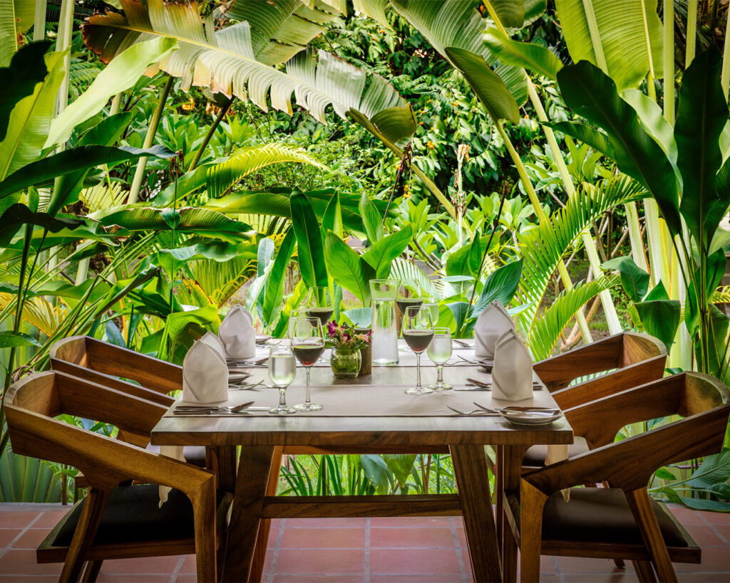 Une table de restaurant dressée au milieu de plantes tropicales.